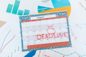 Vibrant August calendar on a desk with deadline marked in red, surrounded by graphs and charts.