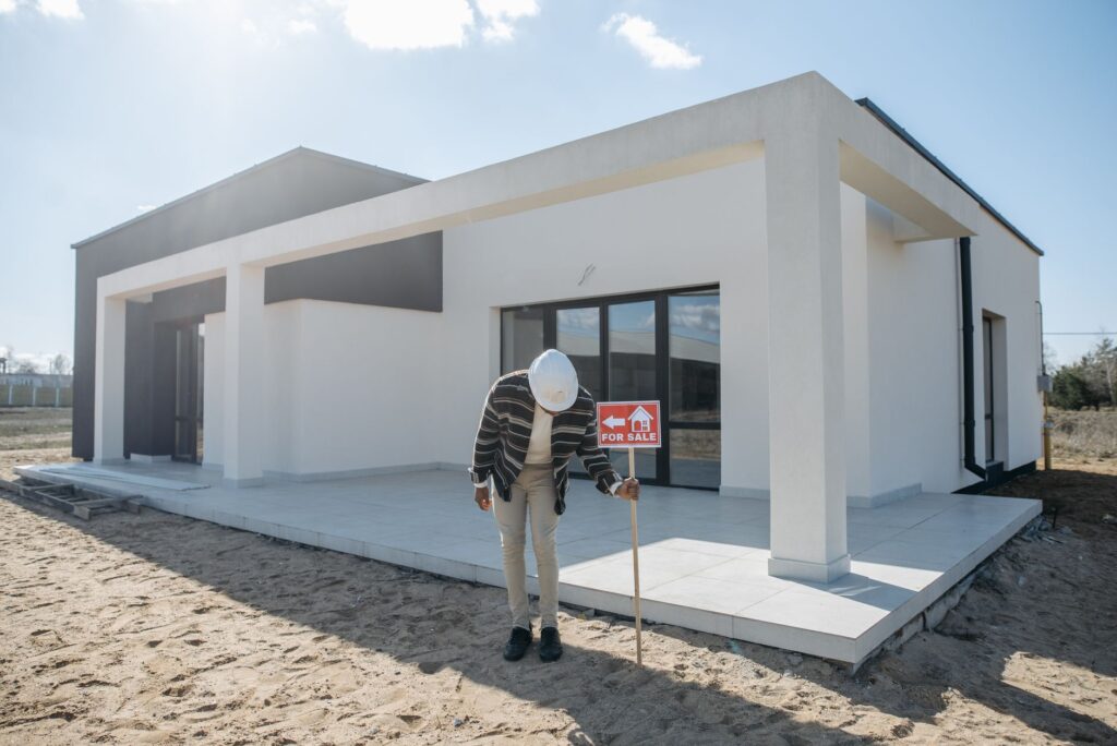 Real estate agent with hard hat standing by a modern house for sale.