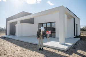 Real estate agent with hard hat standing by a modern house for sale.